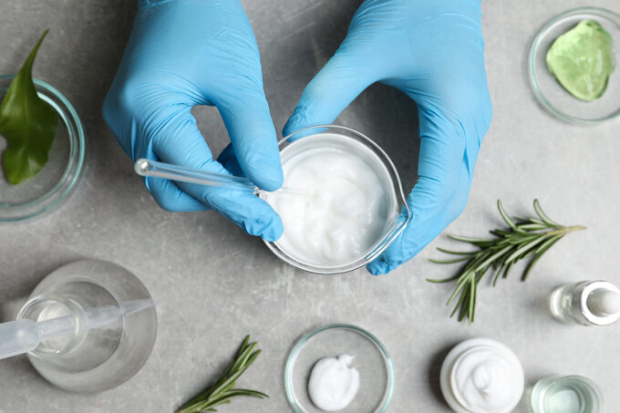 Scientist making cosmetic product at grey table, top view