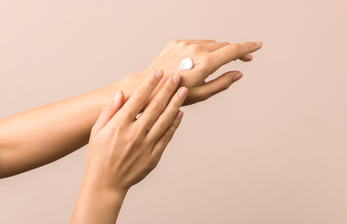 Close-up of female hands against a neutral background while applying a white cream to the back of the hand, symbolizing a blog article dedicated to the most effective dermocosmetics, understanding the skin in depth to improve effectiveness within the Cosmetic & Medical Device business unit of Lifeanalytics.