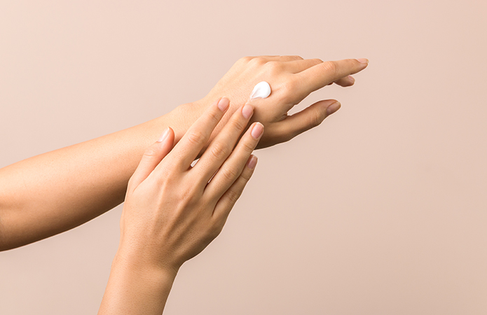 Close-up of female hands against a neutral background while applying a white cream to the back of the hand, symbolizing a blog article dedicated to the most effective dermocosmetics, understanding the skin in depth to improve effectiveness within the Cosmetic & Medical Device business unit of Lifeanalytics.