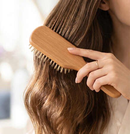 Close-up of a woman brushing long hair with a wooden brush, symbolizing the Lifeanalytics blog article on haircare testing, cosmetic safety assessment, efficacy testing, claim substantiation, and scientific validation for innovative haircare products by the Cosmetic & Medical Device Business Unit